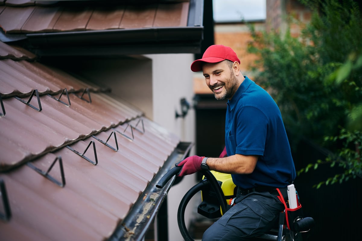 Workman clearing leaves from guttering along a house roof edge